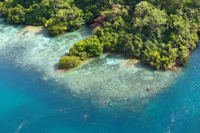 Pulau batu berhutan dikelilingi air laut turquoise